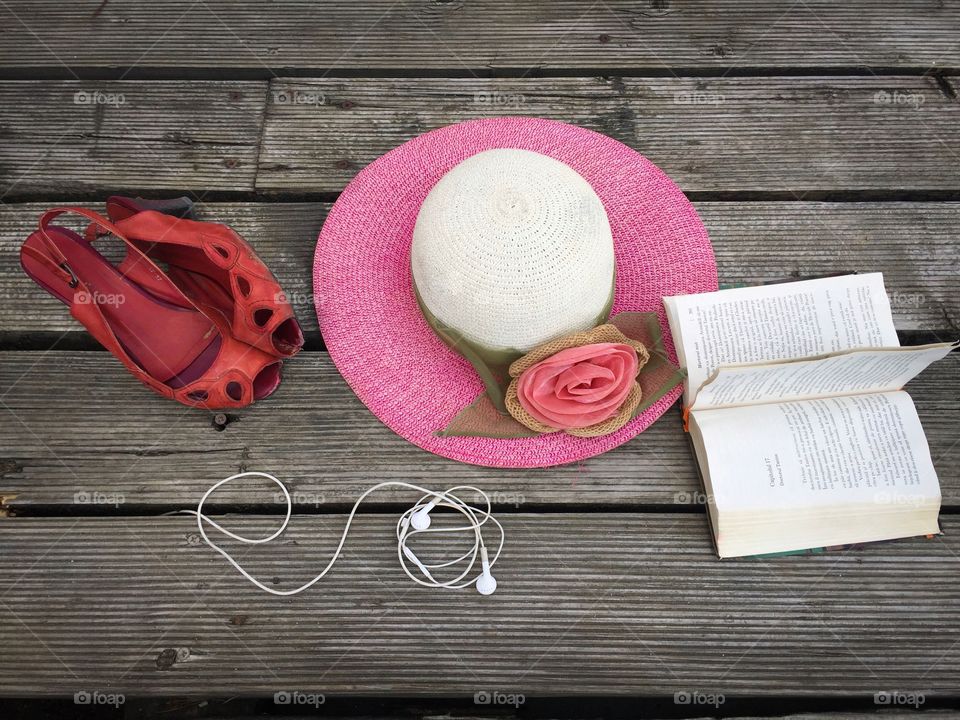 Flat lay summer items on wooden deck: red sandals, hat, book and headphones