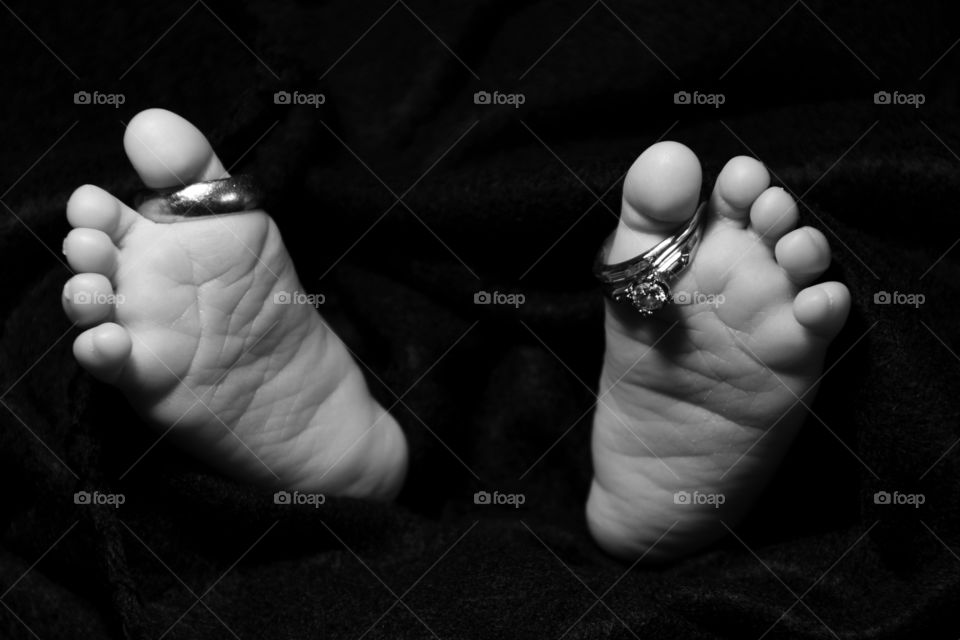 Baby’s feet with wedding rings on big toe. Black and white.