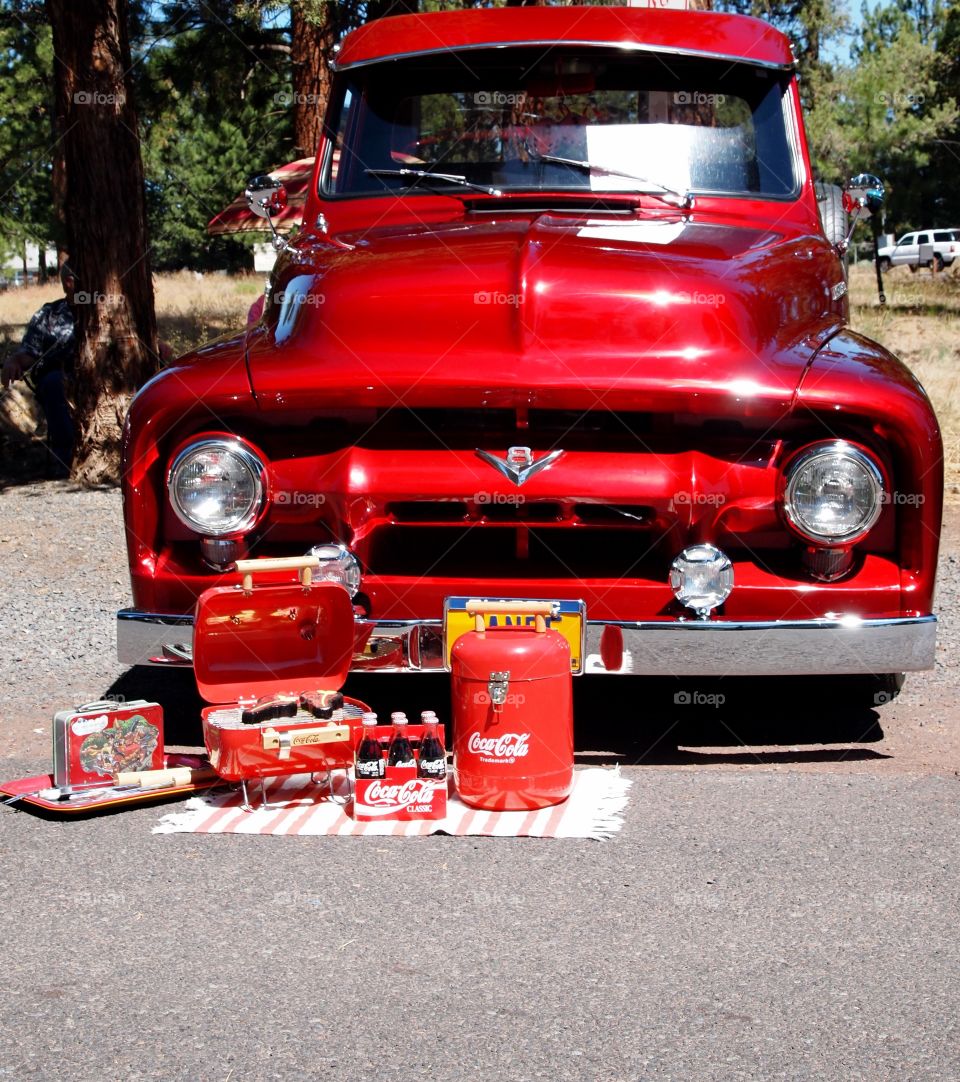A classic truck painted bright cherry red with a Coca Cola picnic display in a park at a festival in Sisters in Central Oregon on a sunny summer day. 