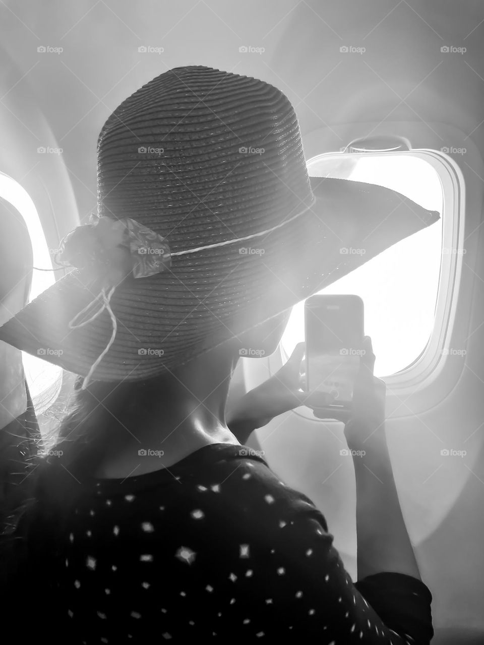 A woman sitting near an airplane window taking a picture of the clouds while traveling. 