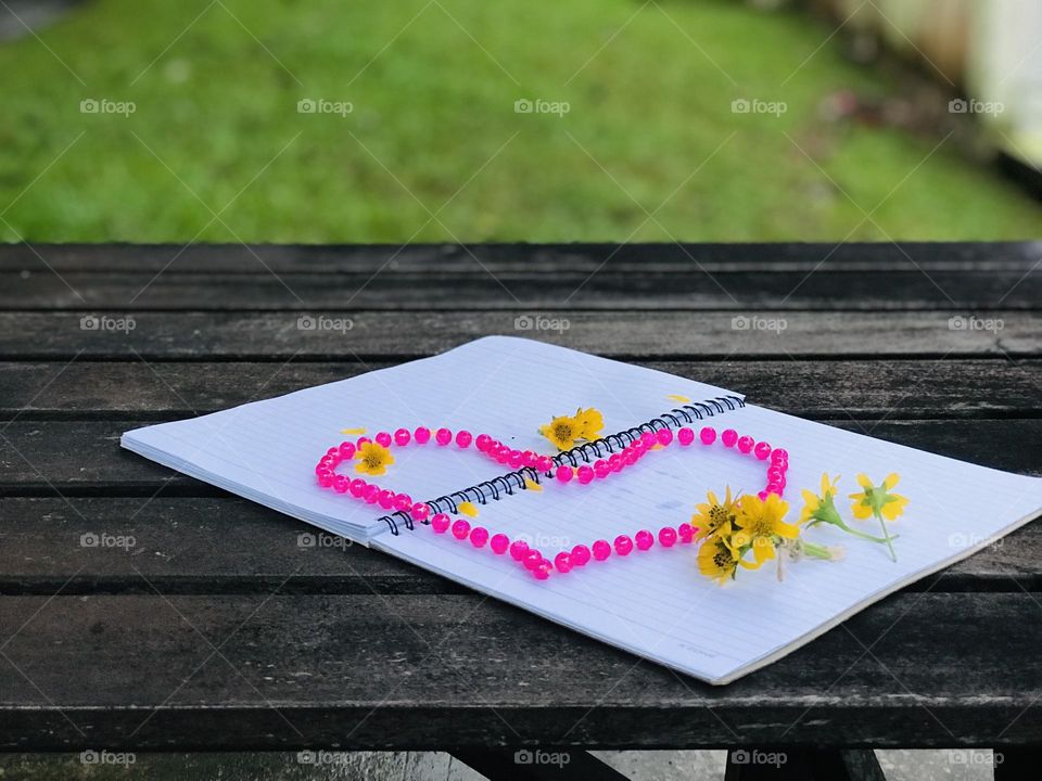 A book with yellow flowers and pink pearl chain on wooden table