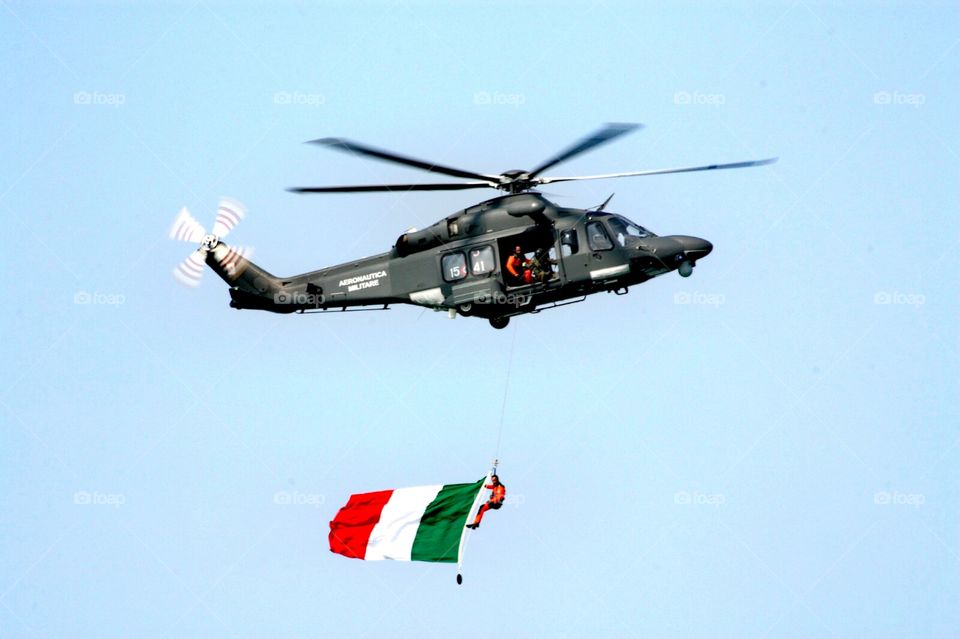 Italian flag hanging from a flying military helicopter