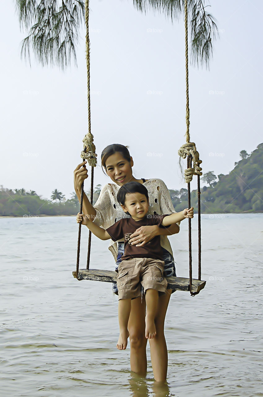 Portrait of mother and son playing swing chair in the sea.