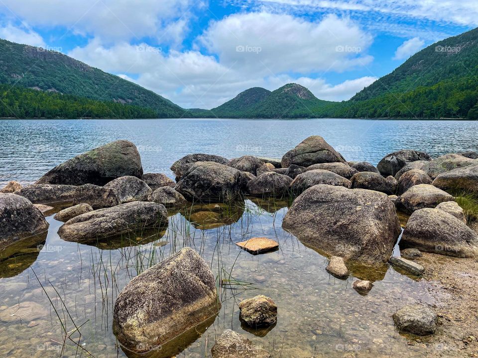 “Jordan Pond.”  Shoreline boulders sit in the tranquil waters while against the backdrop of ‘the bubbles.’