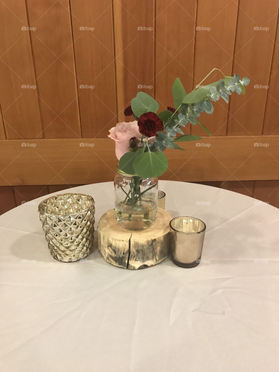 Photo taken at a rustic wedding. This table topper features a pink roses and other plants. Tea light candles set the mood to say I do 
