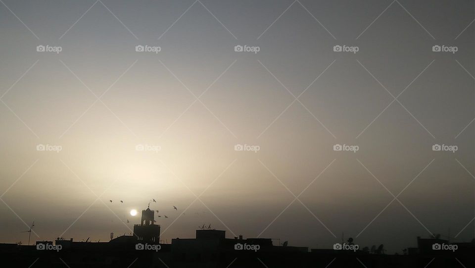 Behind the minaret are flocks of pigeons flying in the sky depositing the sunset.