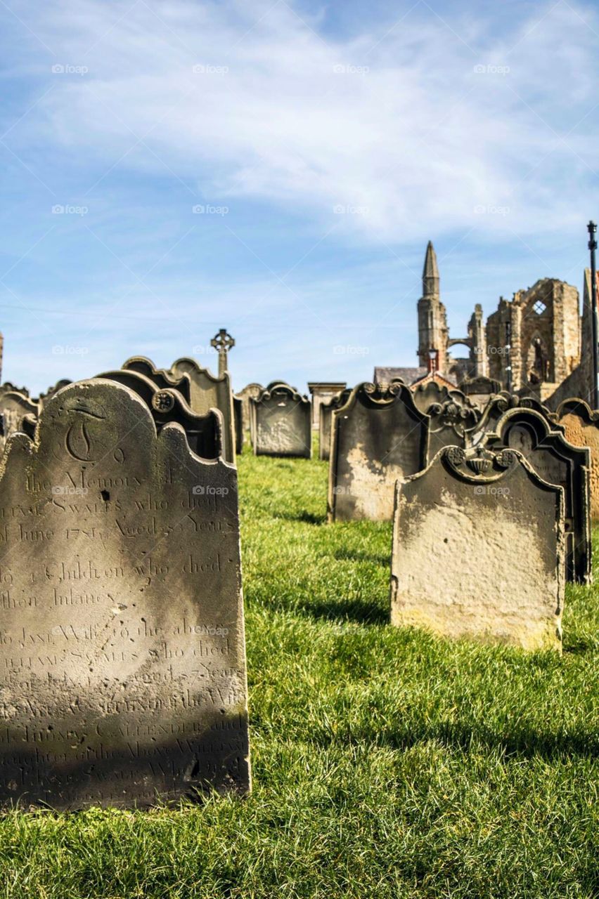 A long gathering of proud gravestones leading the way to historic Whitby Abbey in the distance in this North Yorkshire coastal town in England.