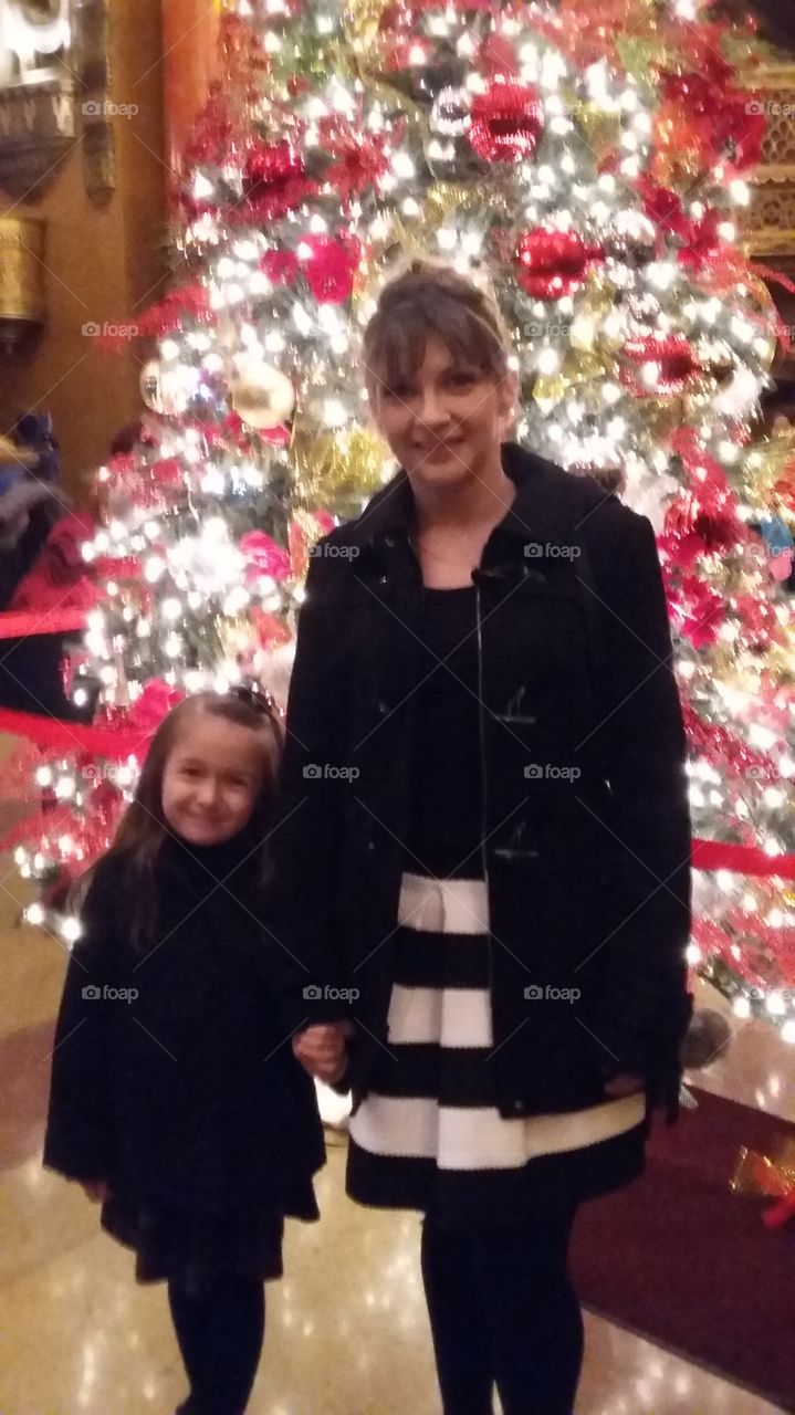 Mother with her daughter standing in front of illuminated christmas tree