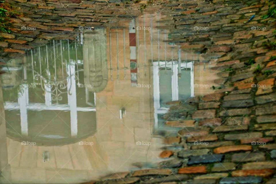 A house in the city is reflected in a puddle on the cobblestones
