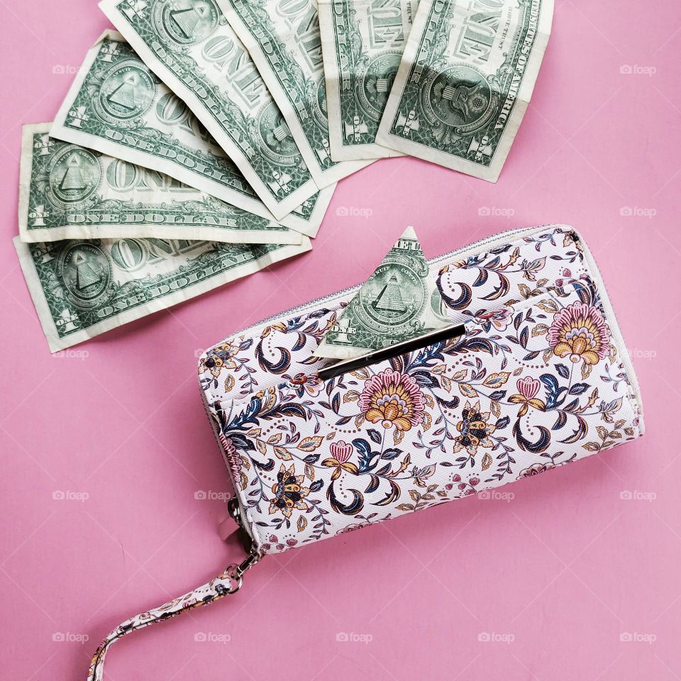 A woman's wallet with a pink pastel design print on a pastel pink background with U.S. dollar bills.