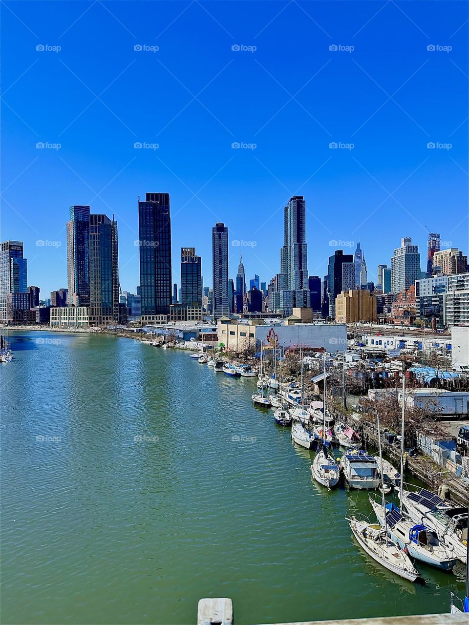 This is beautiful “Newtown Creek” with its great variety of boats seen from the “Pulaski Bridge” that connects LIC, Queens to “Greenpoint”, Brooklyn. Far in the distance we see “Manhattan” incl. the “Empire State Bldg”. 2024. Hypnotic Productions