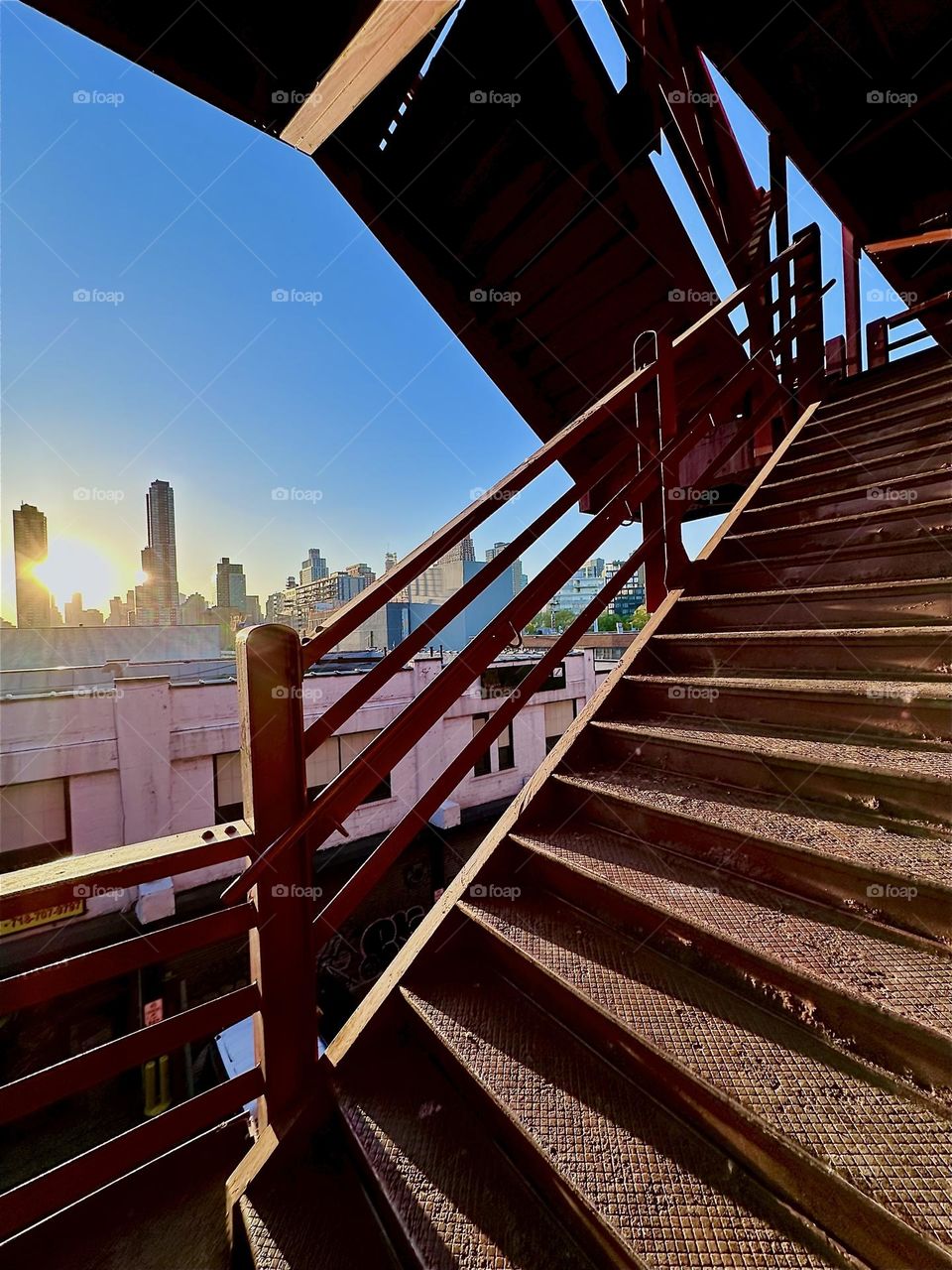This is the red metal staircase of the “Pulaski Bridge” at “Newtown Creek” in LIC, Queens. The setting sun partially illuminates it and turns it into a dark silhouette when photographing against it from a certain angle. 2024. HypnotIc Productions
