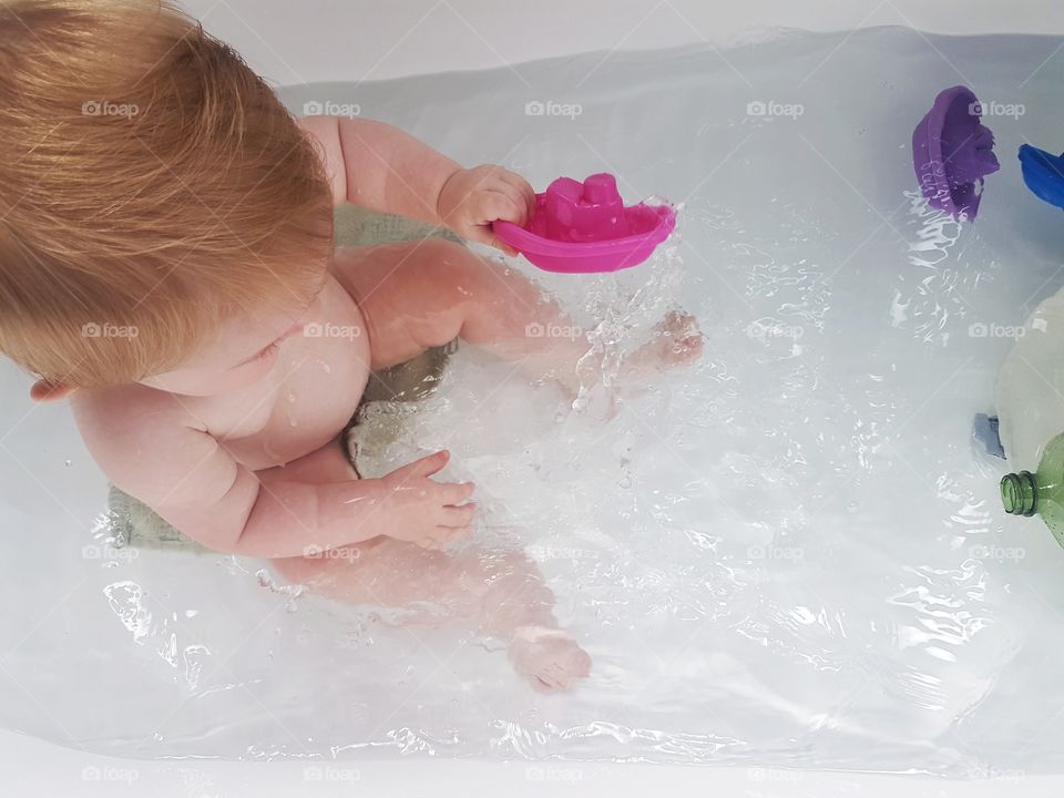 baby playing in the bath water fun colourful boats bathtime wash clean