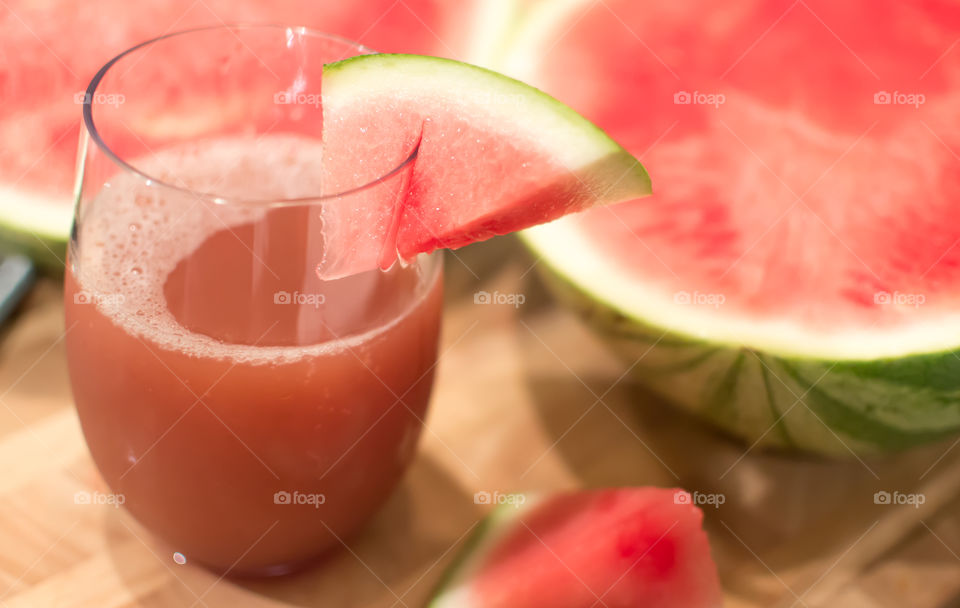 Freshly sliced pink seedless watermelon with home made juice freshly poured in glass on wood table background  healthy summer cocktail and drink photography 
