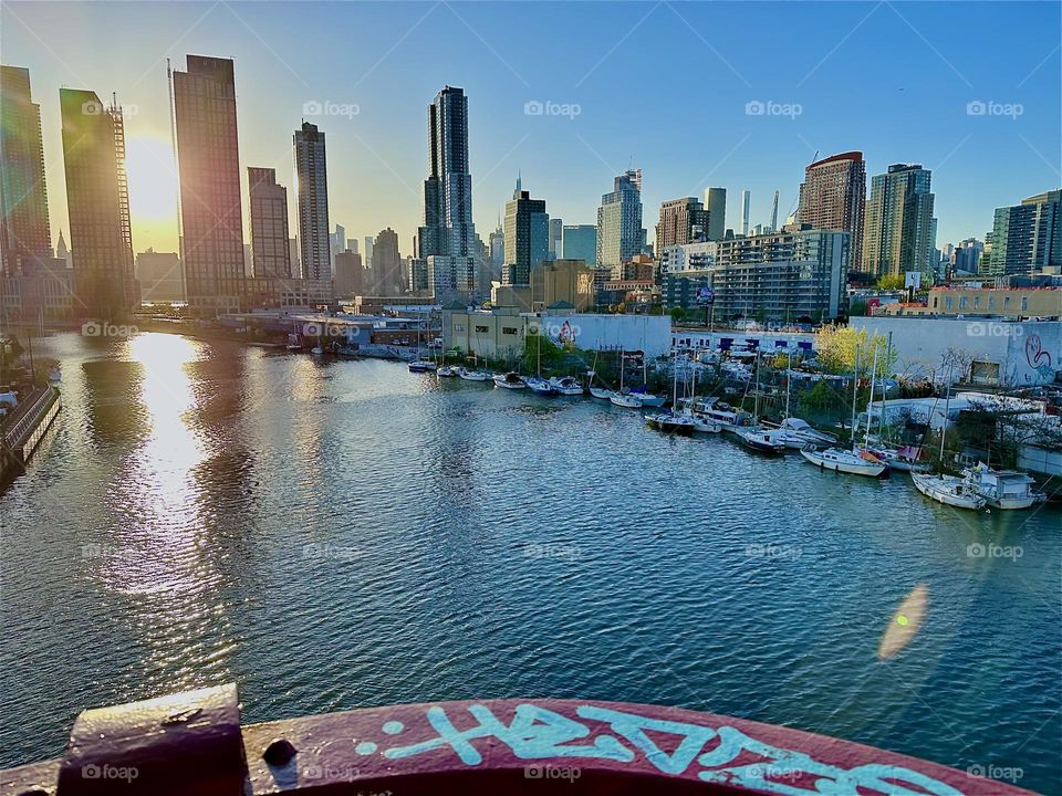 This is “Newtown Creek” seen from the “Pulaski Bridge” that connects “Greenpoint”, Bklyn to LIC with its great variety of boats and magnificent views all the way to “Manhattan” in the intense glow of the setting sun. 2024. Hypnotic Productions