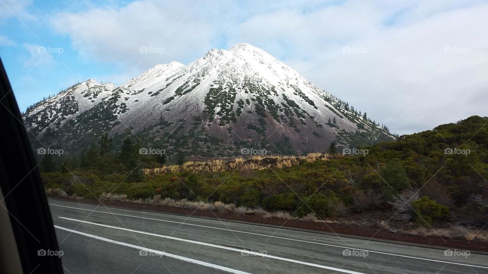 view from a car of a snow-capped mountain against blue sky and gray clouds on a road trip through California