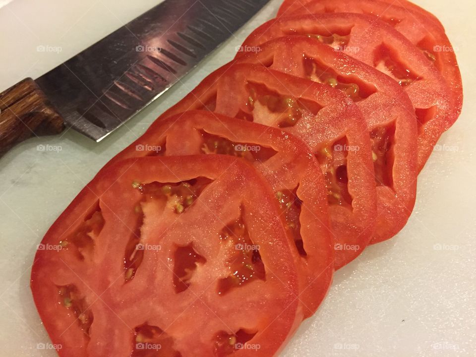 Tomato Slices. Tomato slices and knife on white cutting board