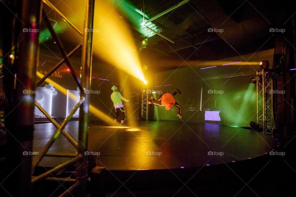 boys in the bright lights of the dance floor perform a complex flip during a hip-hop dance