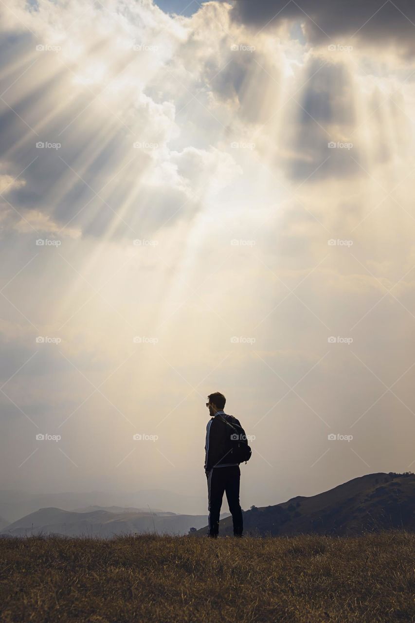 Hiker standing on field against cloudy sky during sunset.