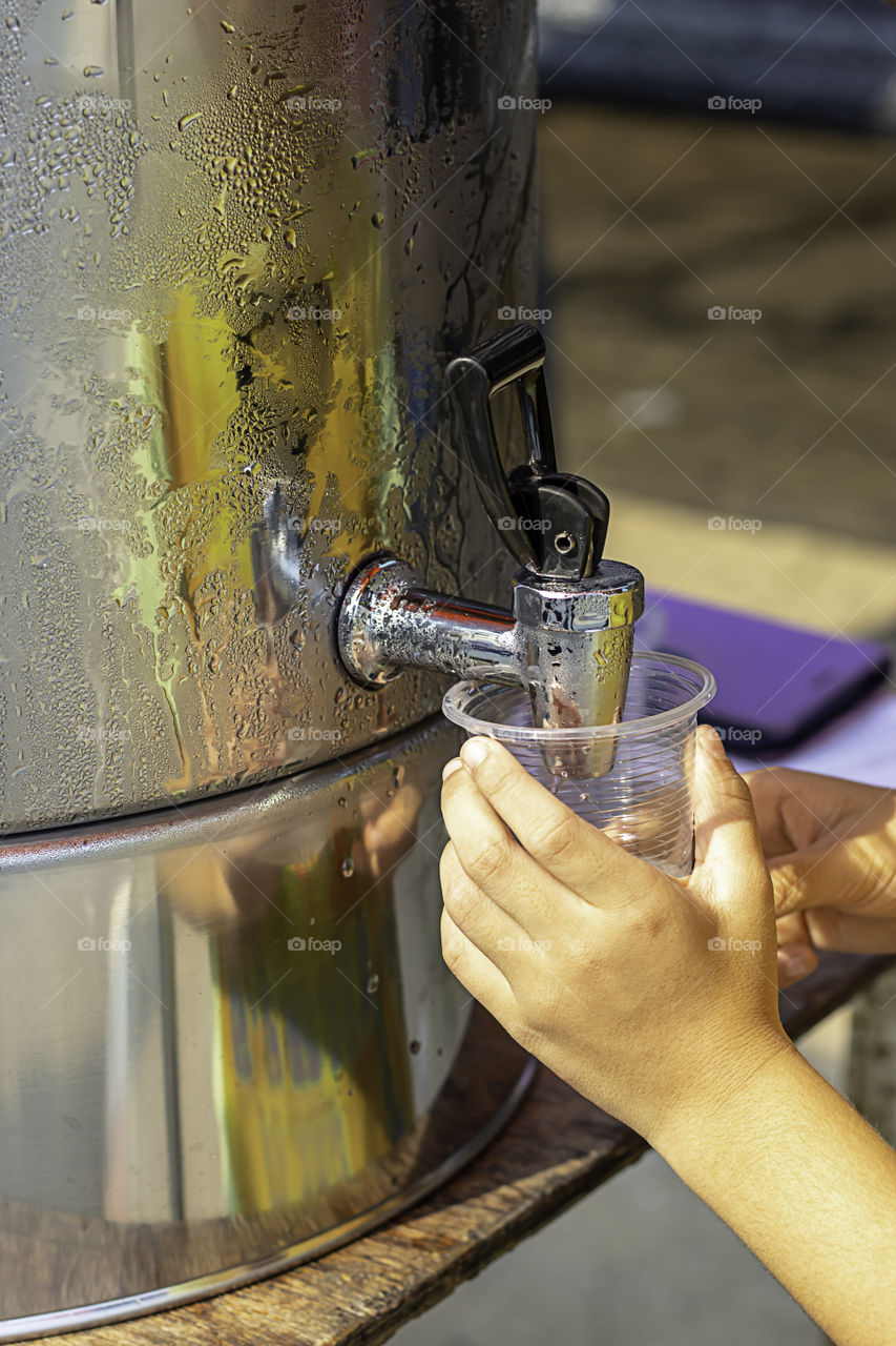 Hand boy holding the glass with water from the water cooler.