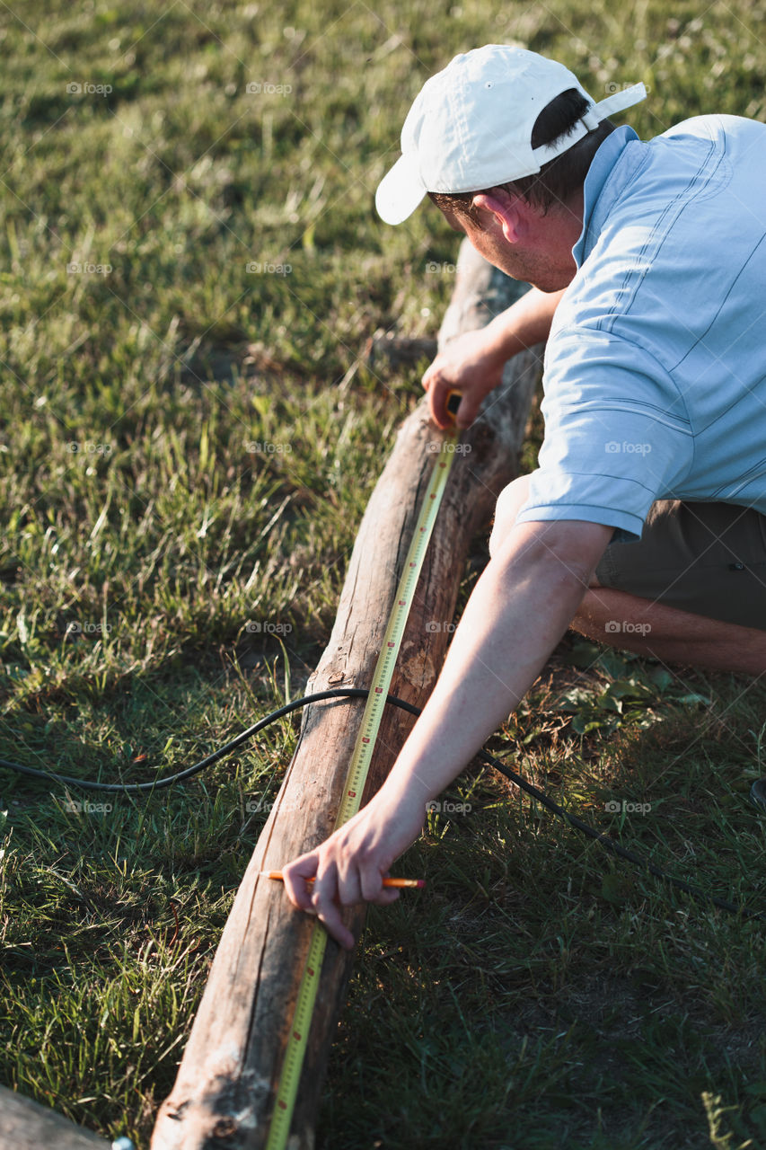 Man using steel tape measure to measuring of timber while working in garden
