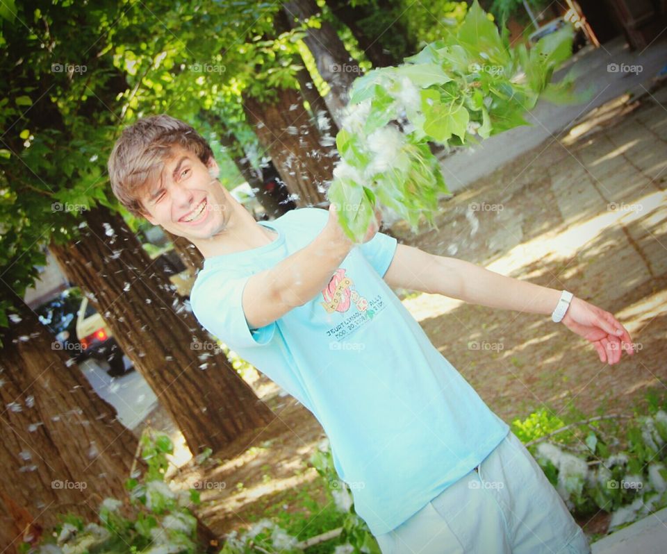 Boy is smiling and is holding branch of poplar. Poplar fluff