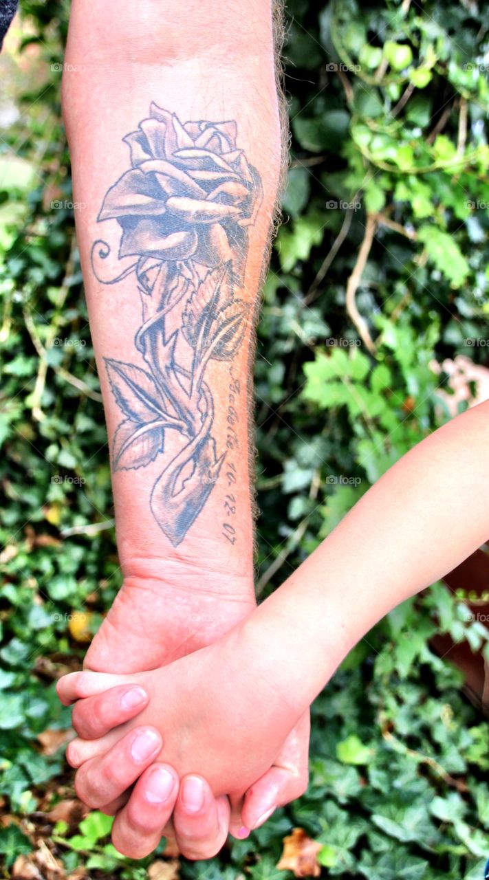 Father holding his daughters hand showing off his rose Tatoo representing his daughter, Isabelle Rose with her birthdate in the Tatoo. She's quite proud of him and honored even at age 8 that he did this! She knows she's always in his heart wherever he is. As her Grandmother, his Mother and the photographer I know how special this photo is!