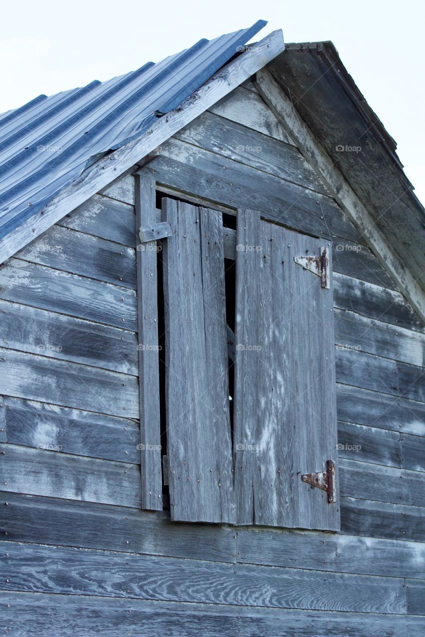 Exterior of a hayloft door with rusted hinges  in the side of an antique farm building  with weathered wood and corrugated metal roof