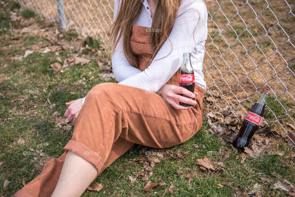 Woman sitting in the grass and holding a bottle of Coca-cola