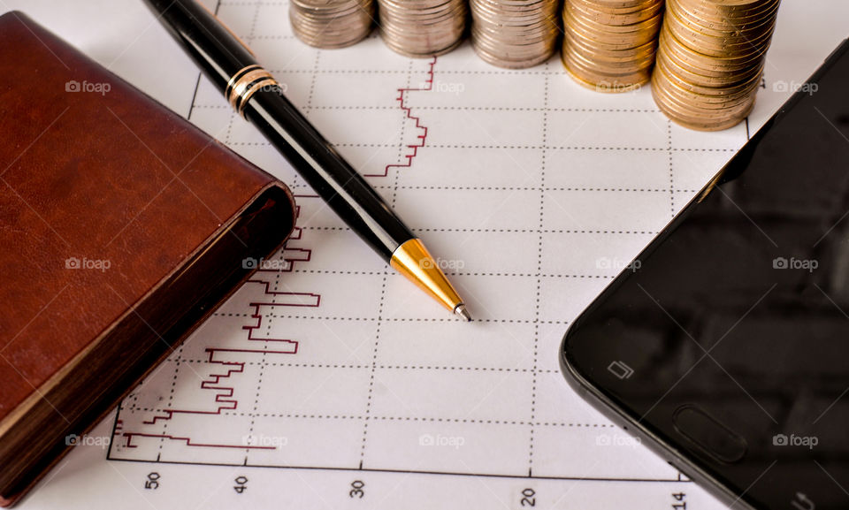ручка блокнот монеты и смартфон на финансовом графике