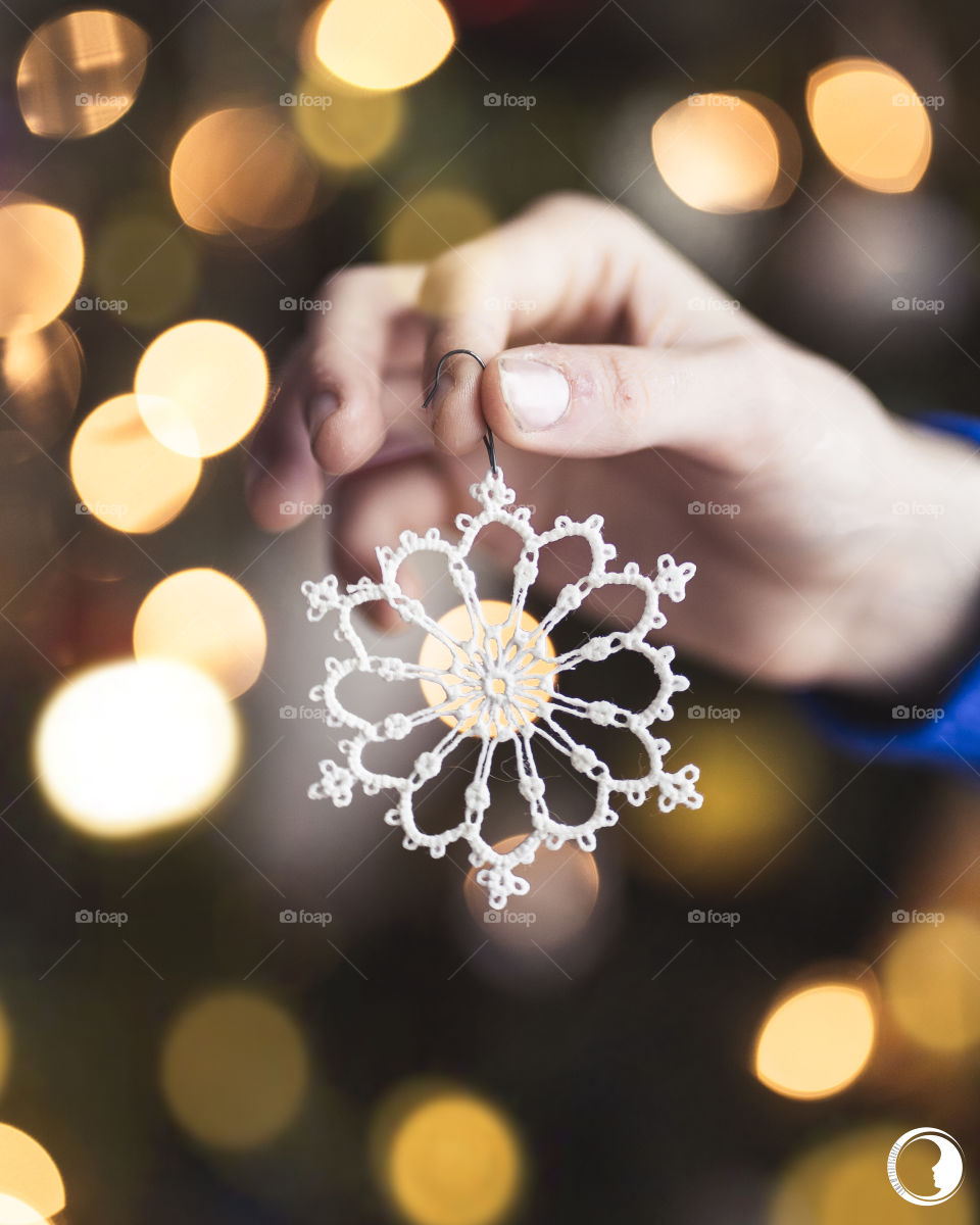 A snowflake ornament in front of Christmas tree full of lights