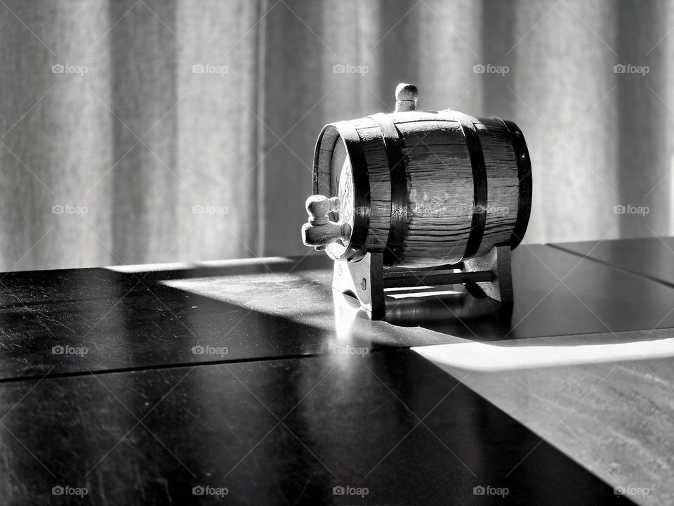Wine barrel on a table illuminated by rays of the sun, taken in the style of black and white.