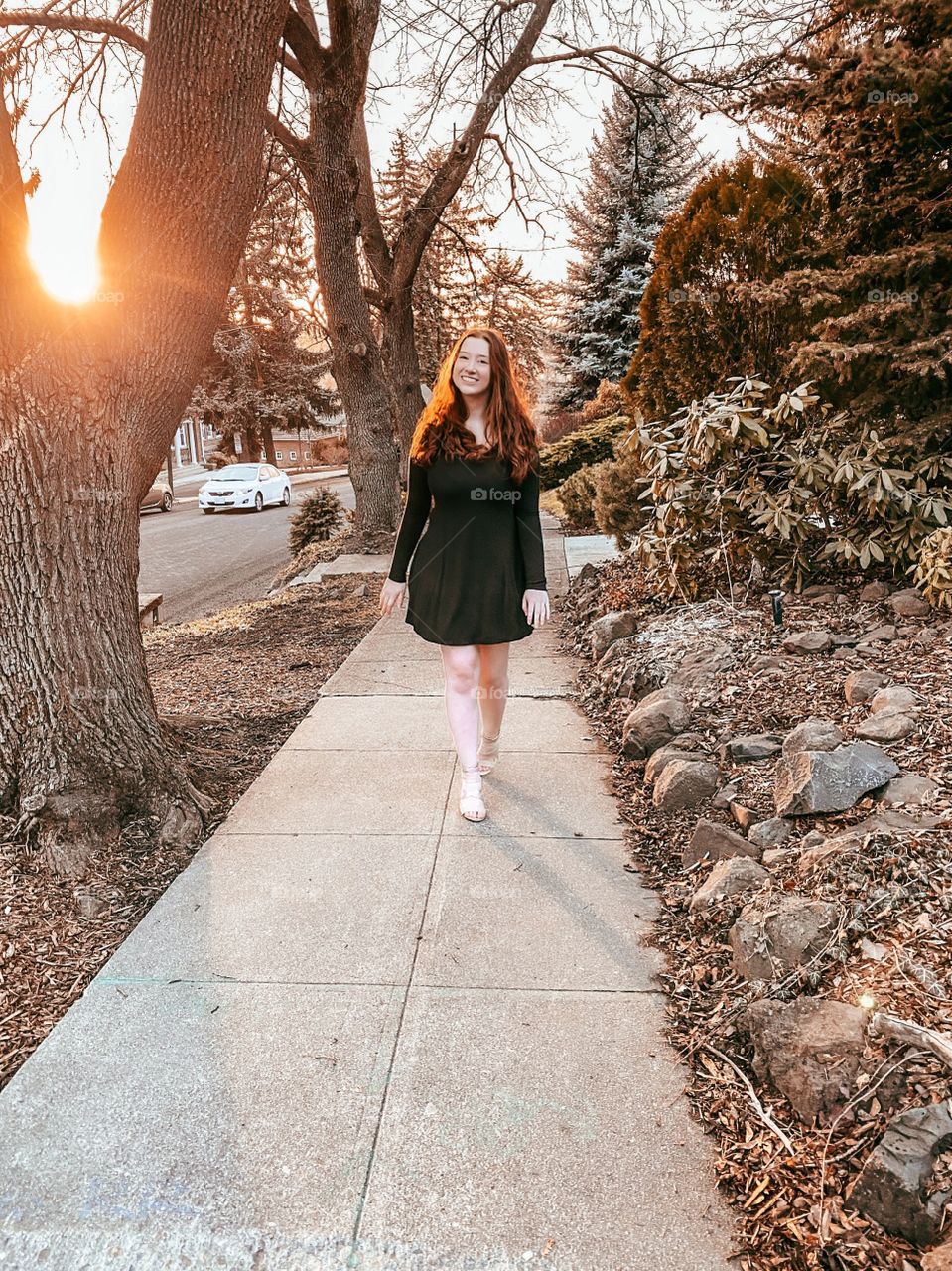 Beautiful image of a walking red-haired model on a decorative sidewalk surrounded by foliage on golden hour