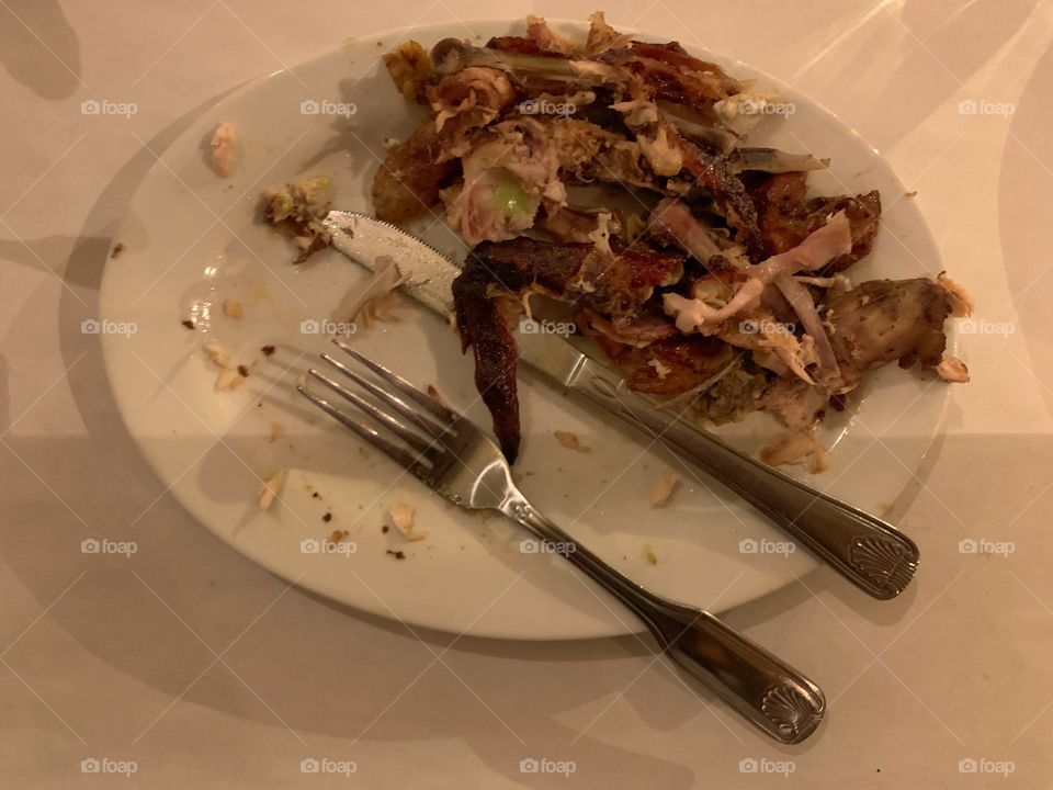 Chicken skin, bones in an oblong white plate. Fork and knife. Results of finished eating.