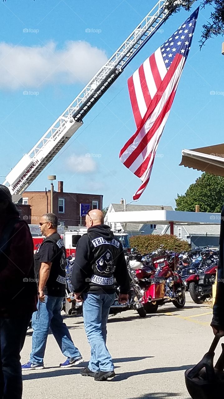 Fire ladder truck with American Flag flying over parking lot in town Center before motorcycle run. Bikers lining up for the ride.