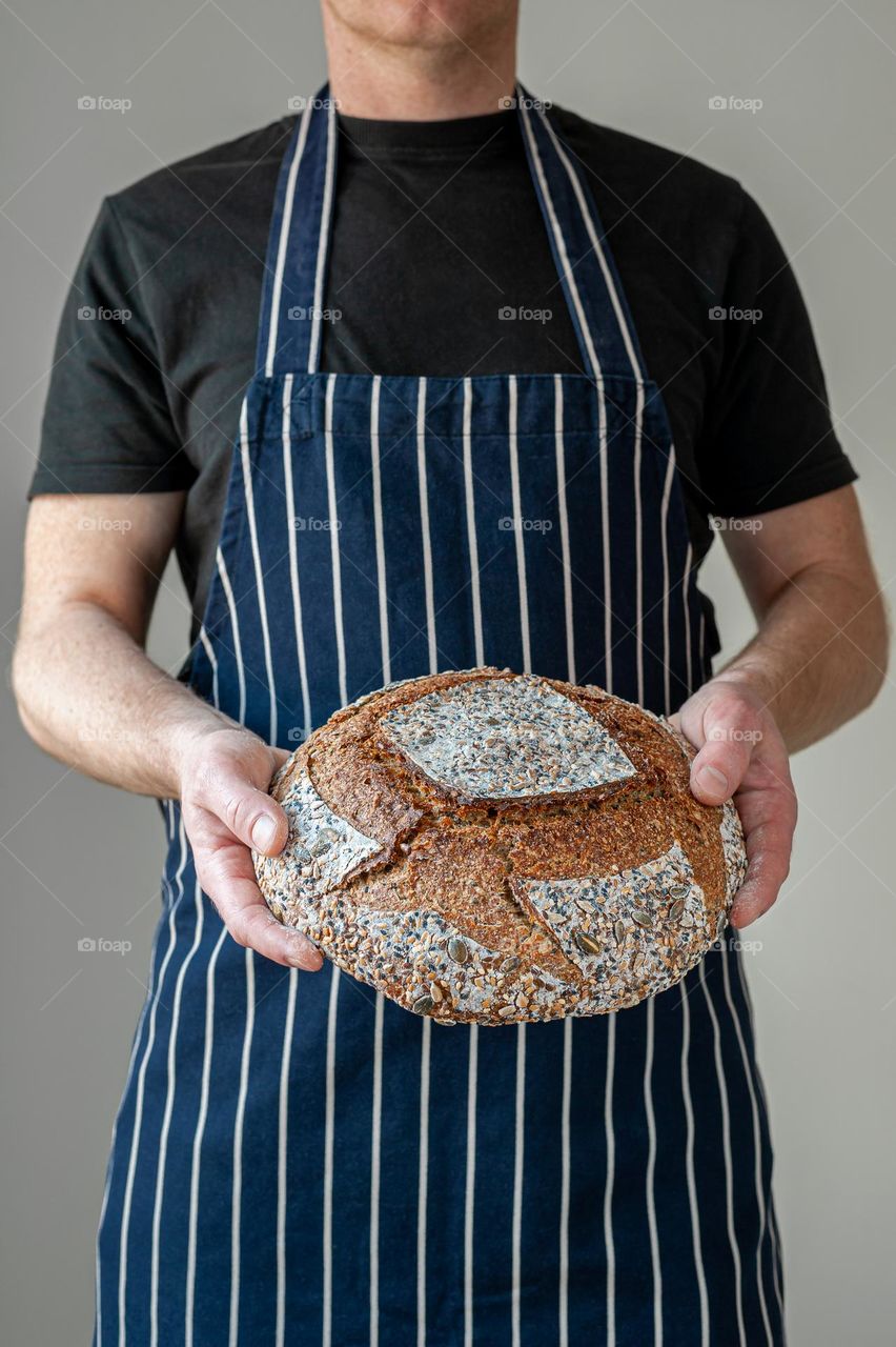 Close-up at bakers hands holding a loaf of sourdough bread in front of him.