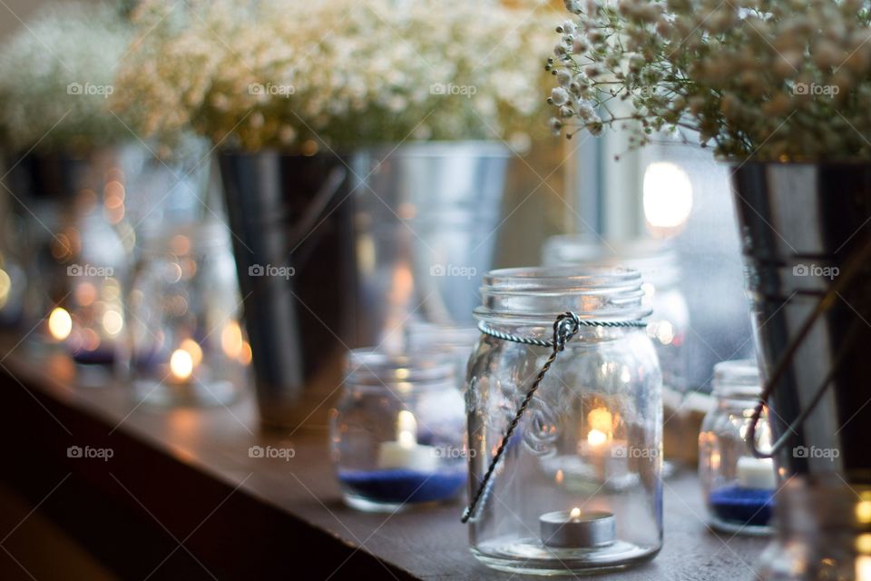 A shelf of candles and vases of baby's breath flowers in front of a window at a reception