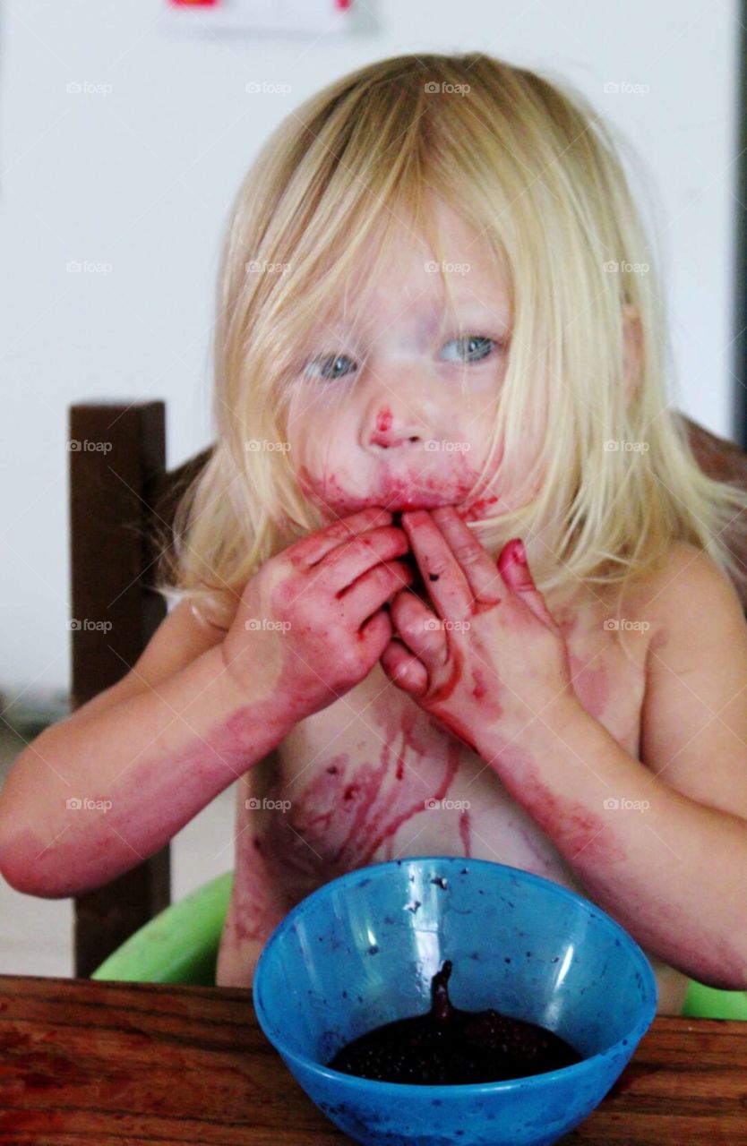 young toddler making a mess while eating blackberries