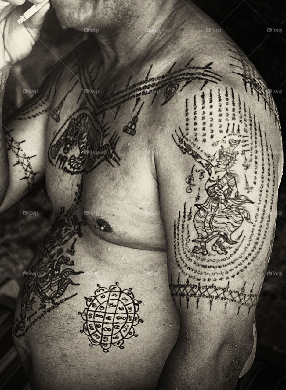 black and white portrait of a man with body coverred with tattoos representing Thai Buddhism and believed to by protector