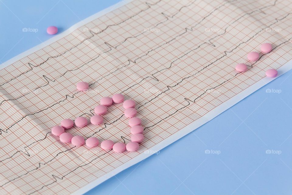 Pills and medicines lie on a blue background with an electrocardiogram of the heart.