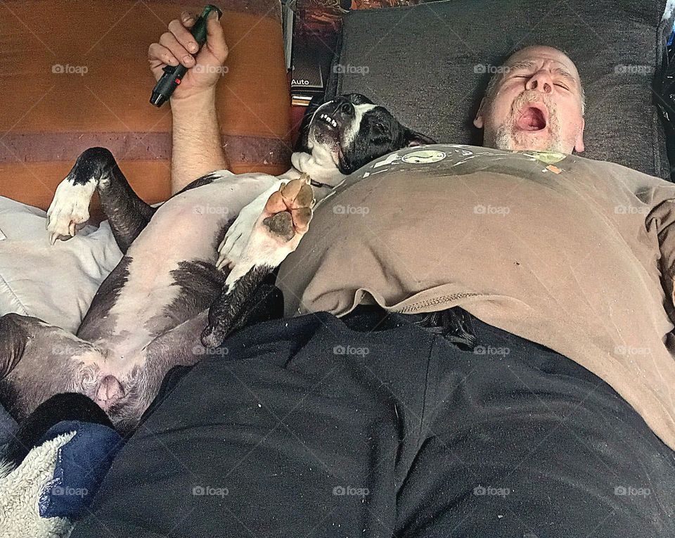 A man, his arm around his best friend, laying together on their backs yawning on a lazy afternoon.