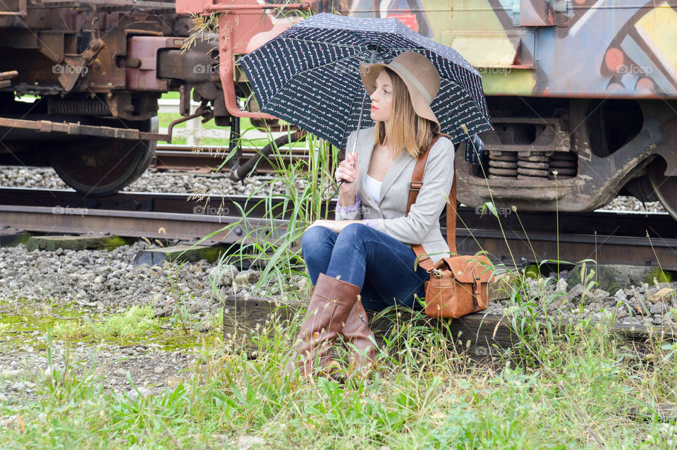 Woman sitting in front of a colorful train car with an umbrella