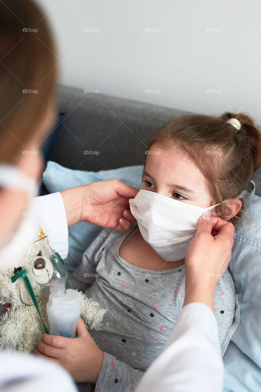 Doctor covering little patient's face with mask. Sick girl having medical inhalation treatment with nebuliser