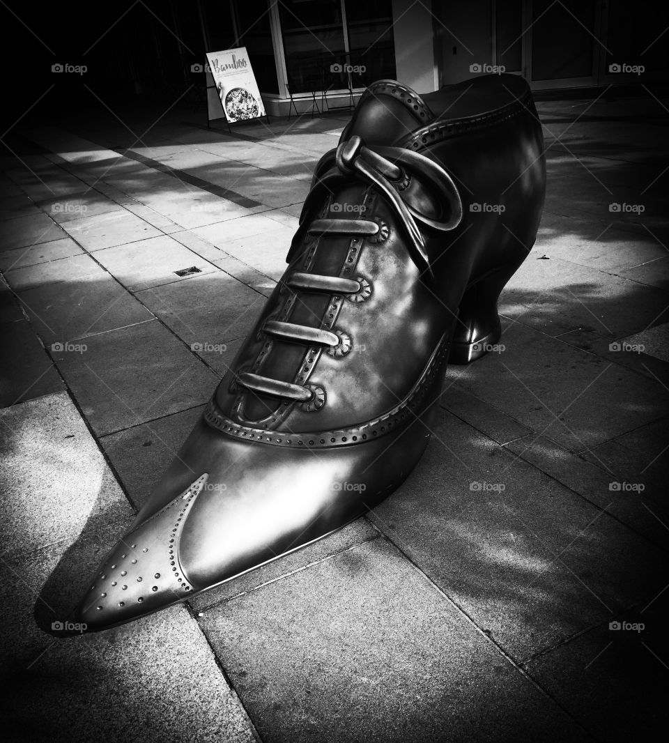 Black and white image of a metal shoe which stands as art outside a shopping mall