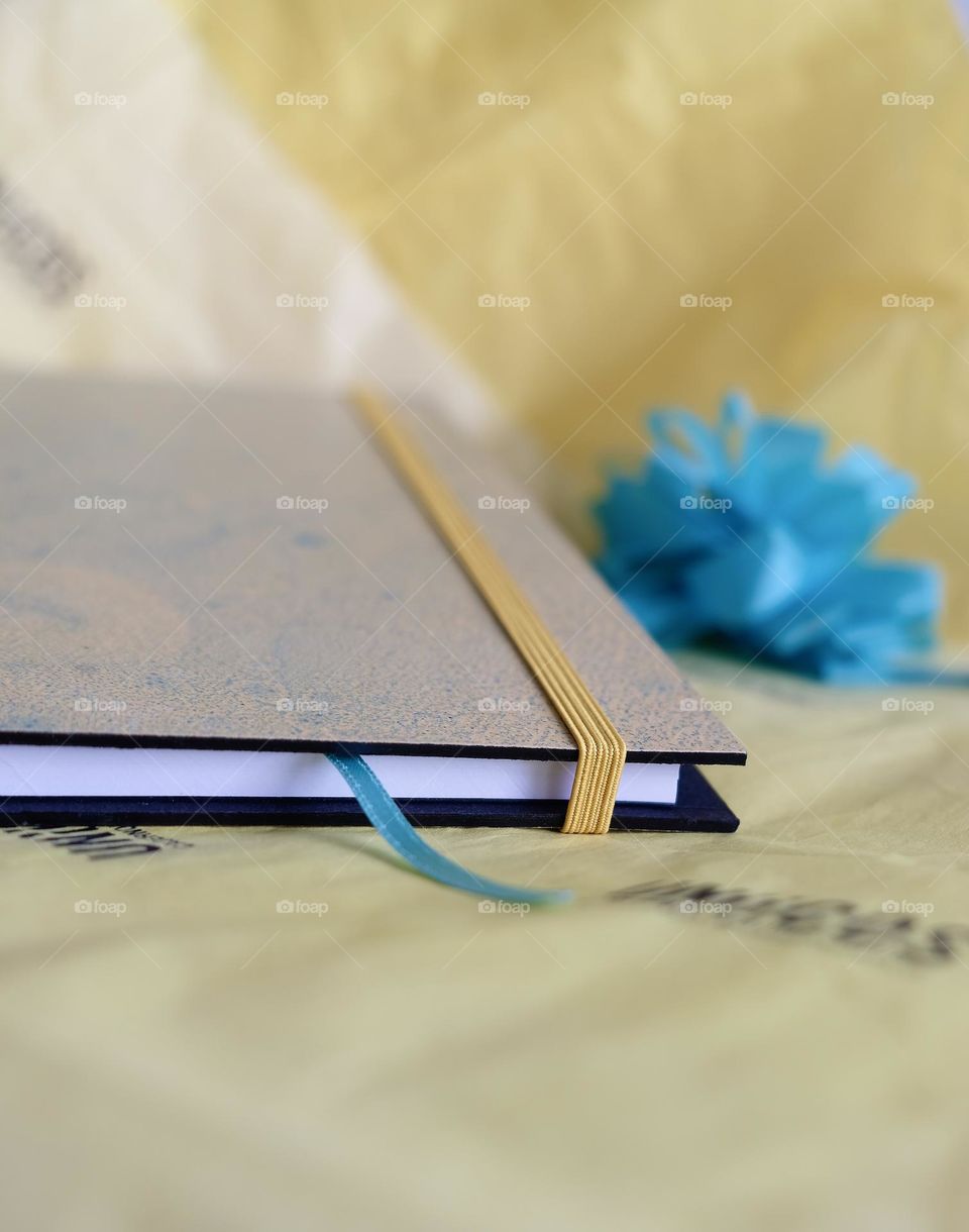 Notebook with a yellow elastic band and a blue ribbon on a yellow background with a blue flower."