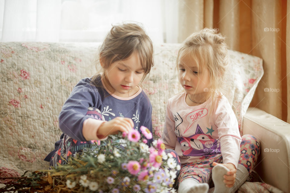 Little sisters in sleepwears with bouquet of autumn flowers at home