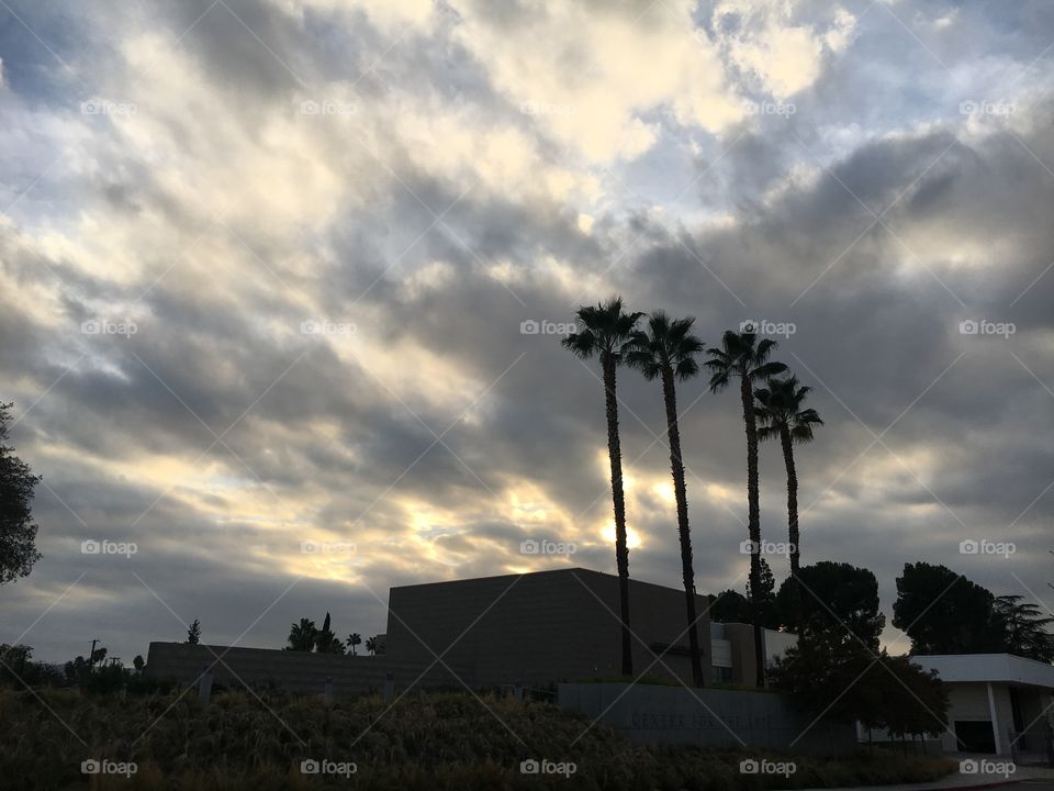 Clouds at sunset over a building and palm trees. 