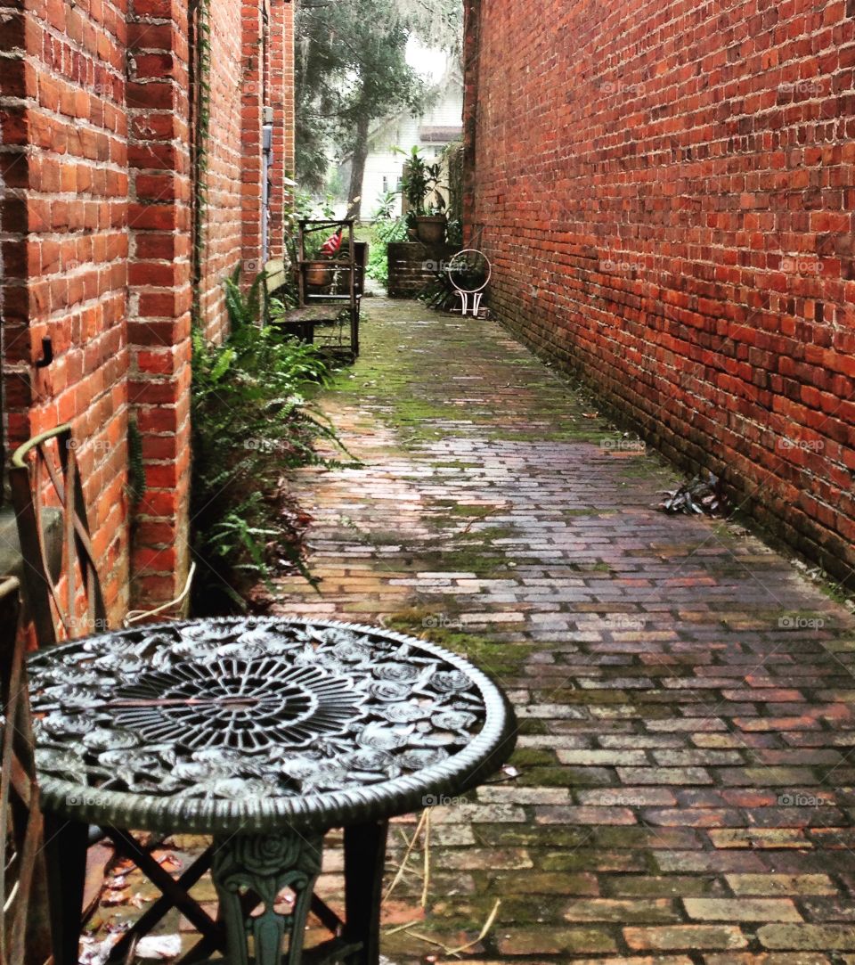 Moss-covered, red brick alleyway with cast iron settee in foreground