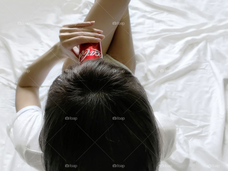 Young woman with long hair drinking cocacola in white bed