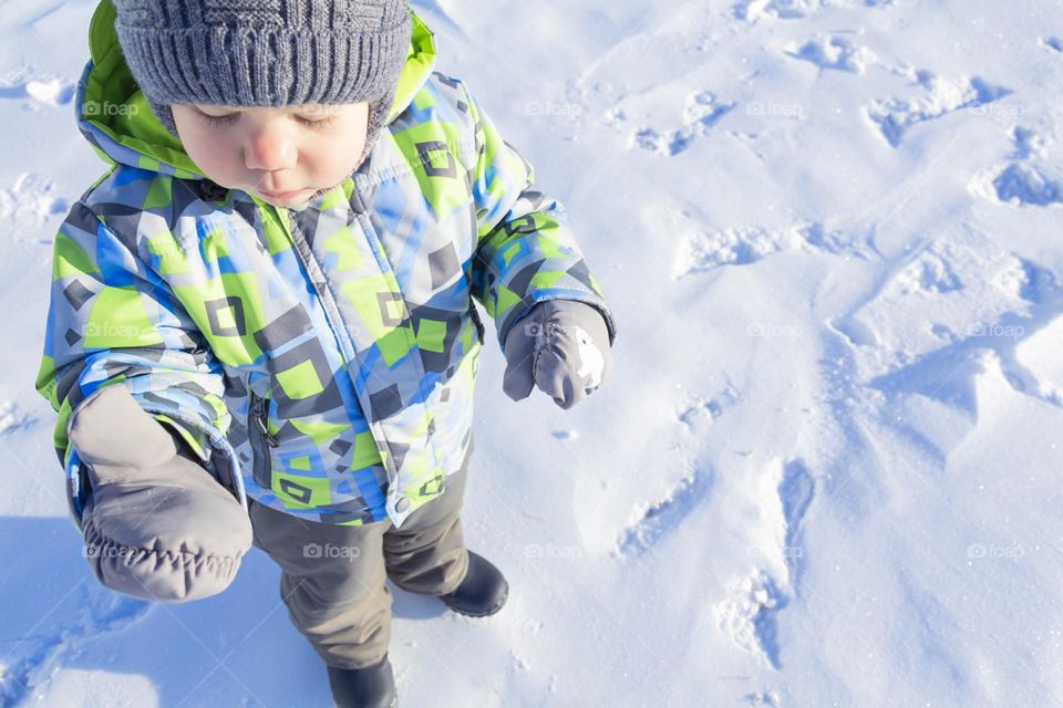 A child with a serious expression on his face in winter clothes jackets, pants, hat and boots in winter on the white snow on the street and in the park in nature plays winter fun.